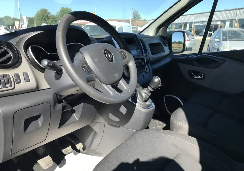 Vue intérieure côté conducteur du Renault Trafic Fourgon blanc 2017, volant multifonction et levier de vitesse manuel visibles.
