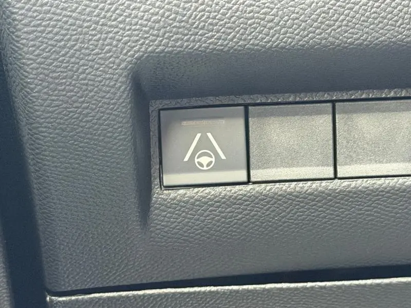 Bouton de commande du système d'aide au maintien de voie sur tableau de bord noir texturé d'un Peugeot 2008 bleu hybride.