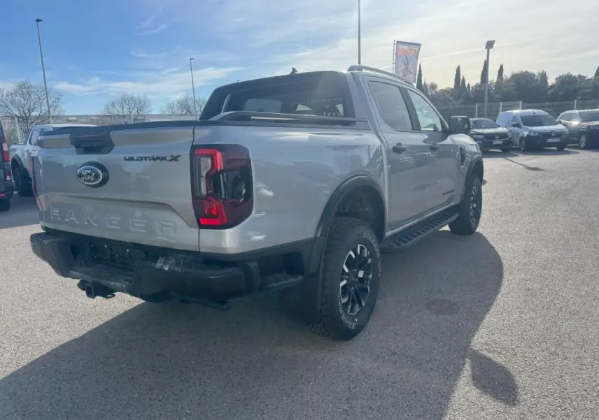 Vue 3/4 arrière droite d'un Ford Ranger gris 2025 Wildtrak X avec jantes alliage et barres de toit visibles.
