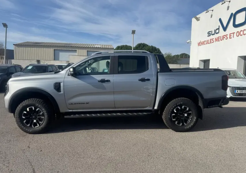 Vue de profil côté gauche d'un Ford Ranger gris 2025 Wildtrak X avec jantes alliage noires et barres de toit.