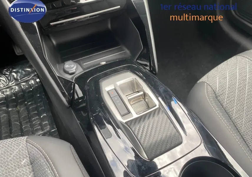 Vue rapprochée de la console centrale noire brillante avec sélecteur de boîte auto et sièges tissu gris de la Peugeot 208 Hybrid 145ch.