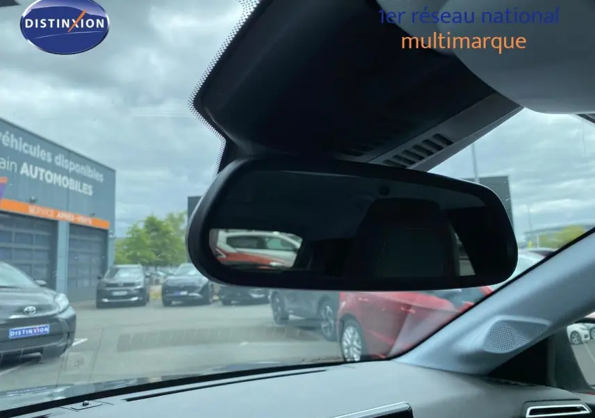 Vue intérieure du rétroviseur central d'une Peugeot 208 gris selenium, avec reflet du parking extérieur et autres véhicules visibles.