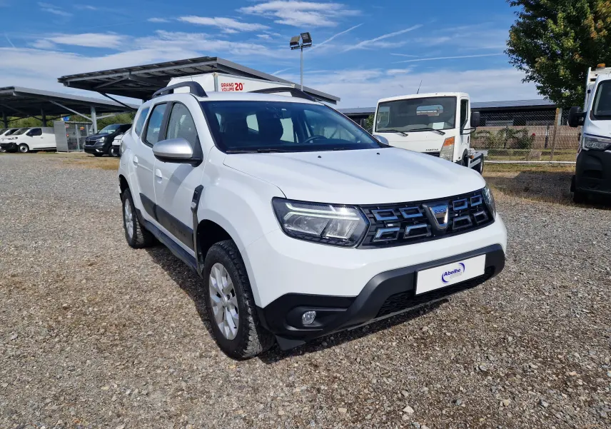 Dacia Duster blanc en 3/4 avant droit, avec calandre noire et protections noires sur les bas de caisse.