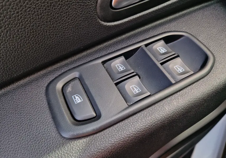 Gros plan sur les commandes de lève-vitres électriques côté conducteur du Dacia Duster 4x4 blanc 2023.