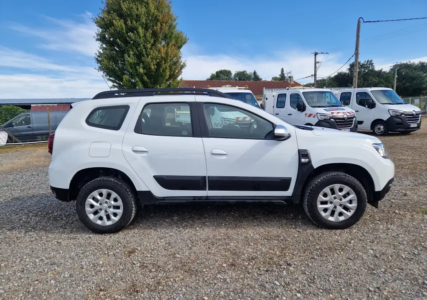 Profil côté gauche d'un Dacia Duster blanc 4x4 2023 avec protections noires et jantes alliage 16 pouces.