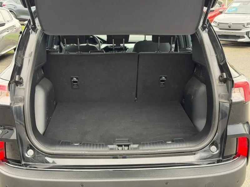 Vue arrière du coffre ouvert d'un Ford Kuga 2024 noir, montrant l'espace de chargement et les dossiers de sièges rabattus.