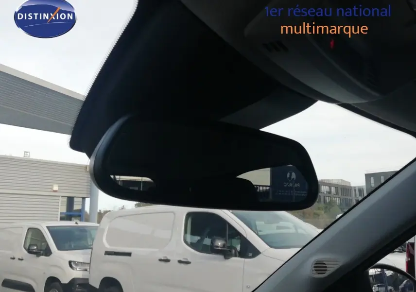 Vue intérieure centrée sur le rétroviseur, avec en arrière-plan un utilitaire blanc visible côté droit.