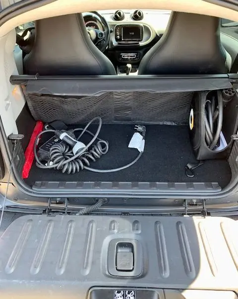 Coffre ouvert d'une Smart Fortwo électrique grise 2019, vue arrière montrant câbles de recharge et intérieur noir.