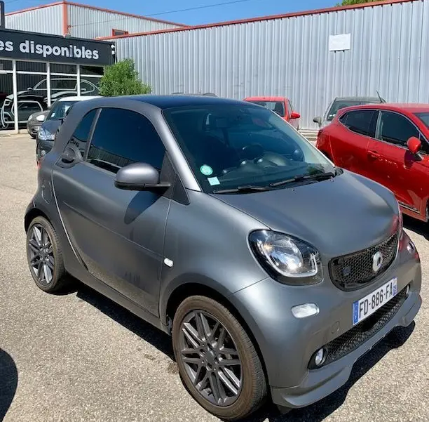 Vue 3/4 avant droite d'une Smart Fortwo Coupé électrique gris mat avec jantes Brabus style sur parking extérieur.