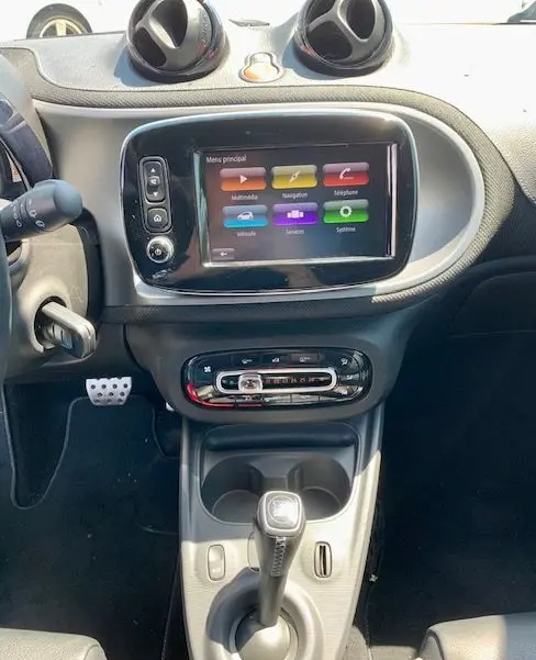 Vue intérieure centrée sur la console centrale d'une Smart Fortwo électrique grise, avec écran tactile et levier de boîte automatique.