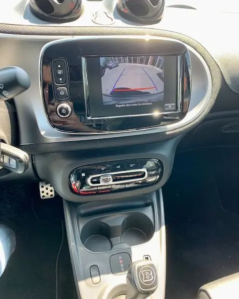 Vue intérieure du tableau de bord et console centrale d'une Smart Fortwo électrique grise, avec écran de recul et levier de vitesses Brabus.