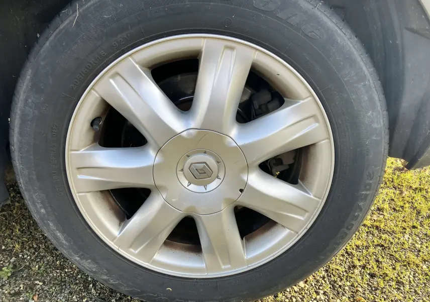 Gros plan sur la roue avant gauche de la Renault Laguna gris vert 2008 avec jante alliage et logo Renault central.