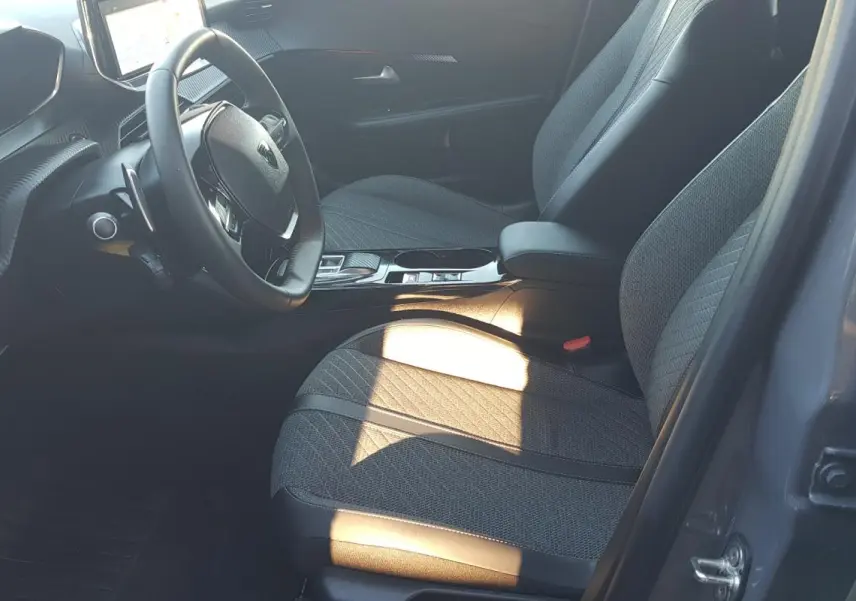 Vue intérieure côté conducteur de la Peugeot 208 Hybrid gris 2024, avec sièges tissu et volant multifonction.