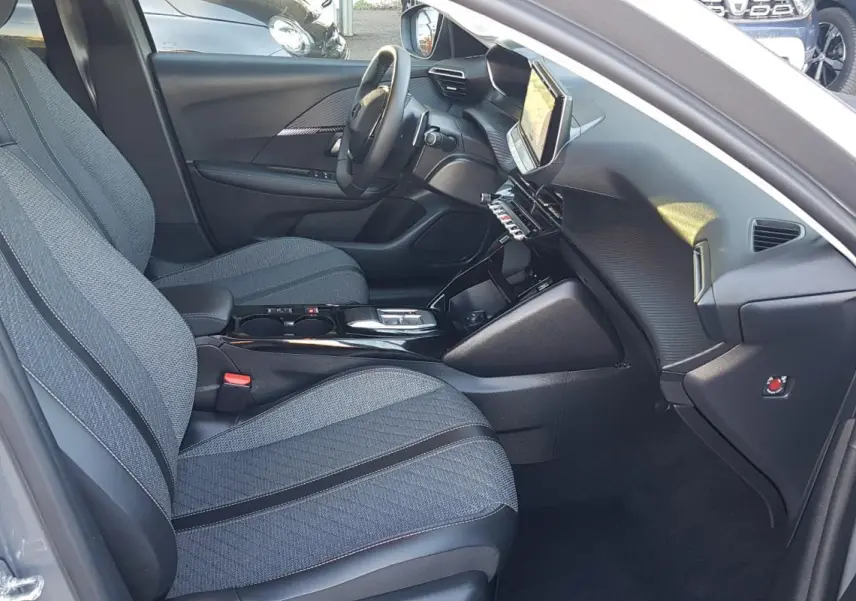 Vue intérieure côté conducteur de la Peugeot 208 Hybrid gris 2024, avec sièges tissu et écran tactile central.