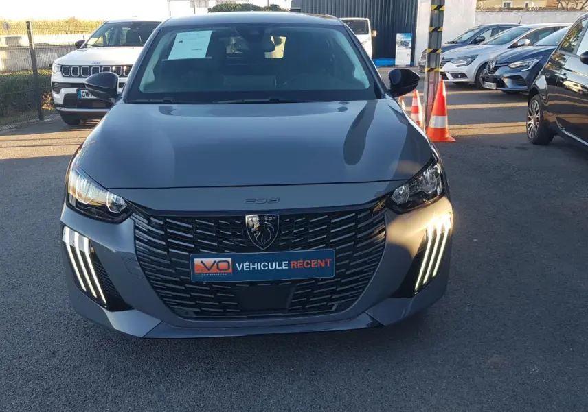 Vue de face d'une Peugeot 208 gris métallisé 2024 avec feux diurnes LED en forme de griffes et calandre noire distinctive.