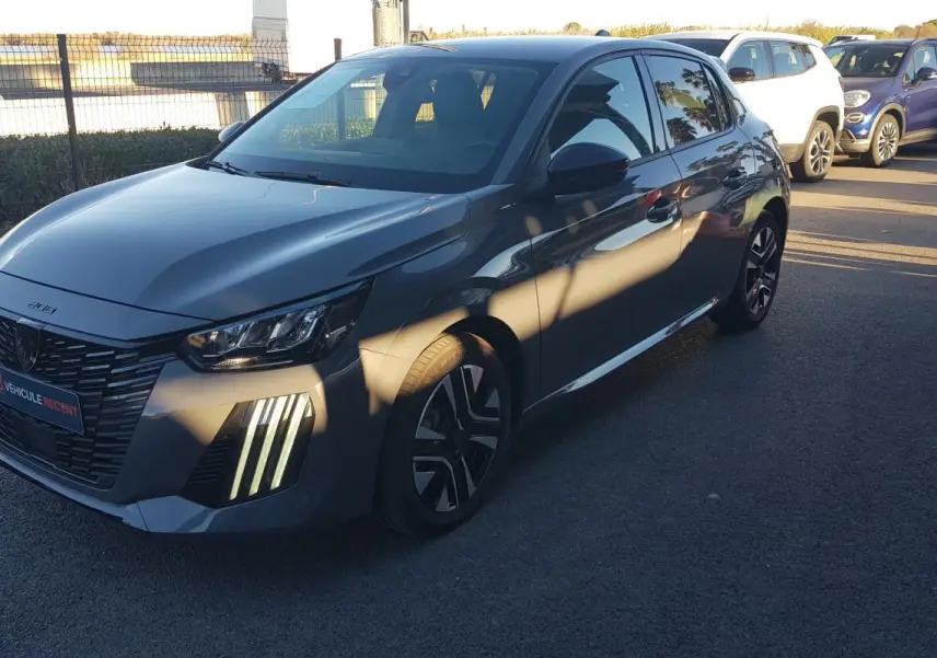 Peugeot 208 gris vue 3/4 avant droit, avec feux diurnes verticaux allumés et jantes alliage 16 pouces.