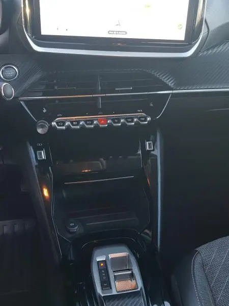 Vue rapprochée du tableau de bord et console centrale noire du Peugeot 208 Hybrid 100 e-DCS6 Allure 2024 avec écran tactile et levier de boîte auto.