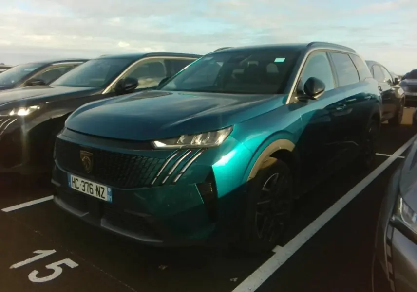 Peugeot 5008 bleu foncé vue 3/4 avant droit sur parking, calandre noire avec griffes LED distinctives.