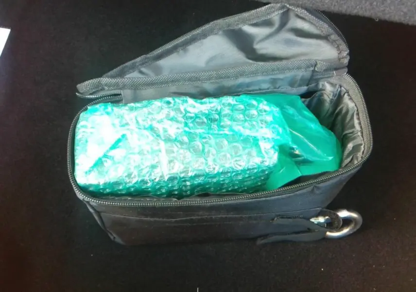 Intérieur du coffre avec sac noir ouvert contenant un objet emballé dans un film à bulles bleu-vert.