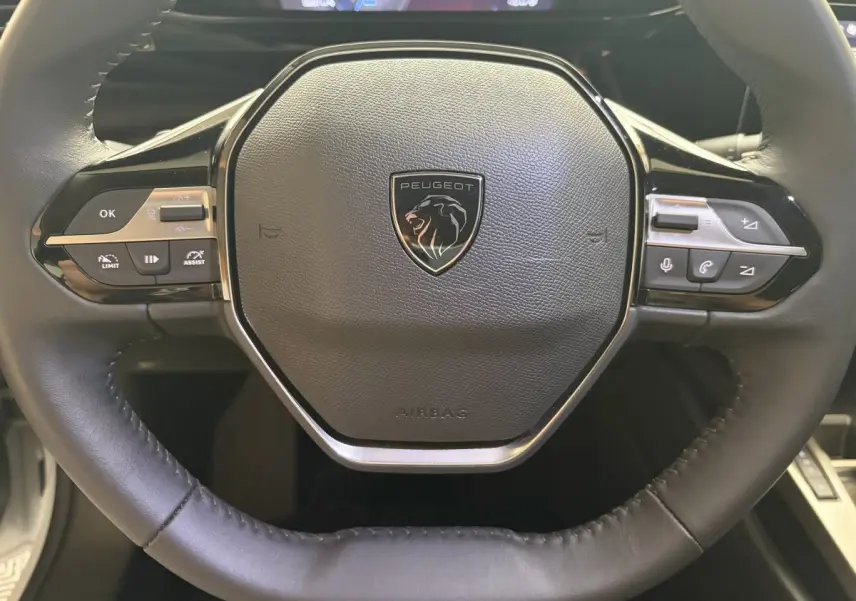 Gros plan sur le volant cuir multifonctions de la Peugeot 308 2024, avec logo lion central et commandes intégrées.