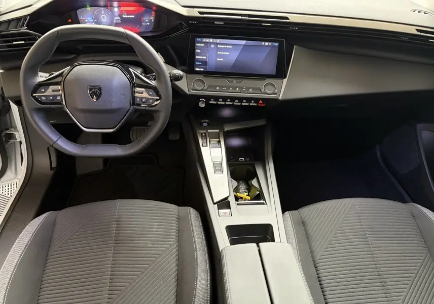 Vue intérieure avant de la Peugeot 308 blanche 2024, montrant le volant cuir multifonctions et l’écran tactile central.