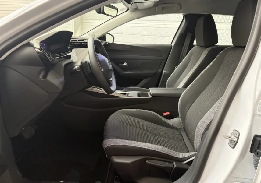 Intérieur avant de la Peugeot 308 blanche 2024, vue côté conducteur, sièges tissu noir et gris, tableau de bord moderne.