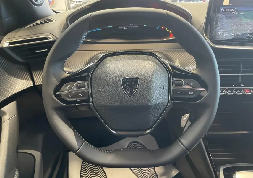 Vue rapprochée du volant compact cuir noir avec commandes intégrées, tableau de bord et écran tactile du Peugeot 2008 hybride 2026.