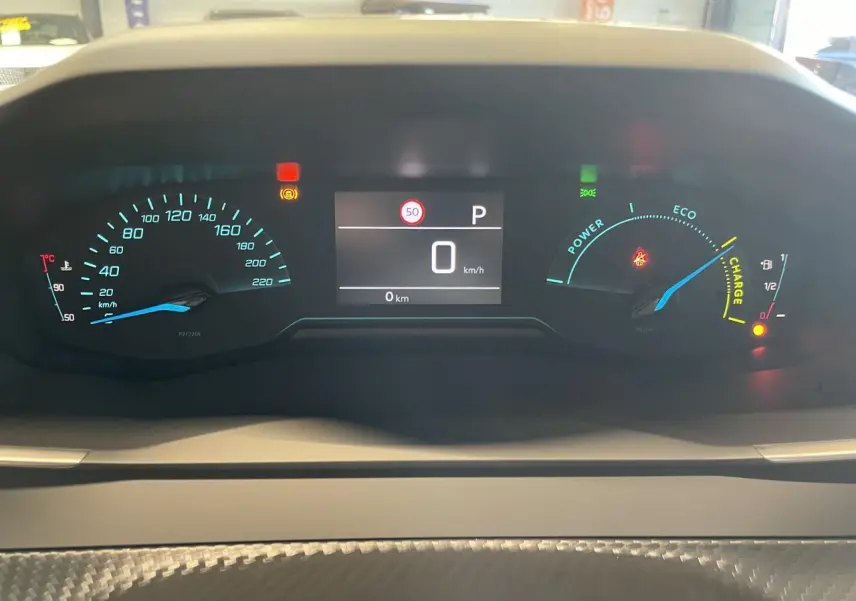 Vue rapprochée du combiné d'instruments numérique du Peugeot 2008 hybride blanc, affichant 0 km/h et indicateurs de charge et vitesse.