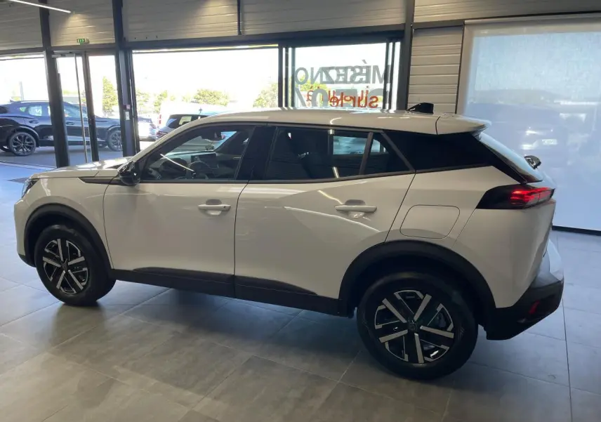 Peugeot 2008 blanc vue de profil côté gauche en intérieur, avec jantes noires et feux arrière LED allumés.