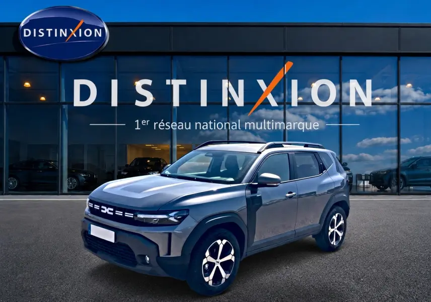 Dacia Duster gris schiste en 3/4 avant droit, avec jantes alu et barres de toit, devant une vitrine Distinxion.