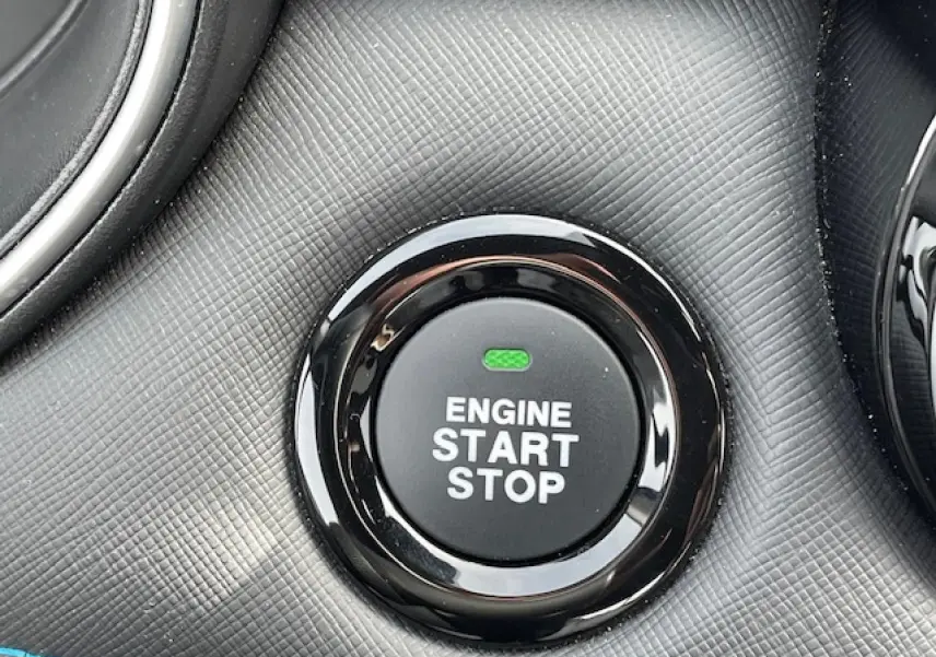 Gros plan sur le bouton noir brillant "Engine Start Stop" entouré d'une surface texturée gris foncé du tableau de bord.