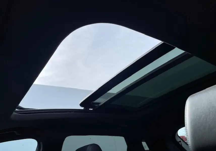 Toit panoramique ouvert vu de l'intérieur sur une SERES 3 Luxury noir métal avec ciel bleu visible.