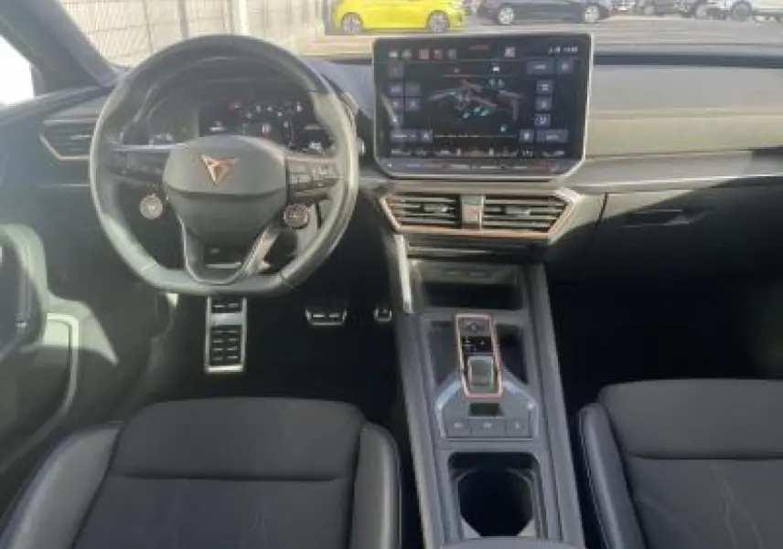 Vue intérieure avant de la CUPRA Leon 2025, volant cuir, écran tactile HD et console centrale moderne en noir.