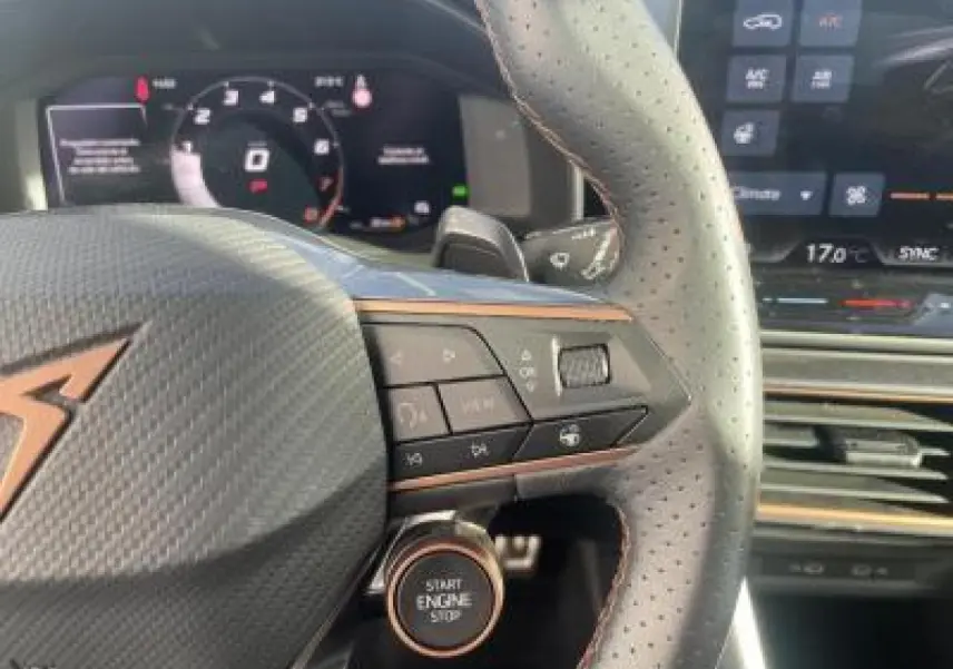 Gros plan sur le volant en cuir perforé avec logo CUPRA et bouton start/stop, tableau de bord digital en arrière-plan.