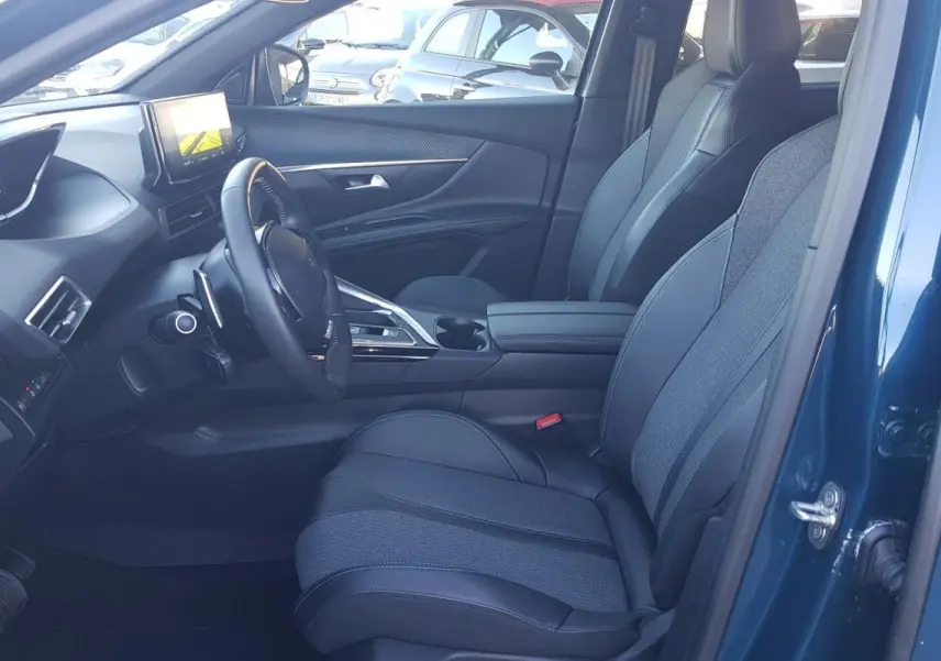 Intérieur côté conducteur du Peugeot 5008 bleu 2024, avec sièges tissu-cuir, écran tactile et volant cuir visible.