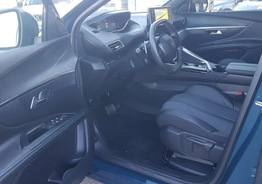 Vue intérieure côté conducteur du Peugeot 5008 bleu 2024, avec volant cuir, écran tactile et sièges réglables.