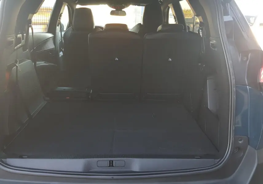 Coffre ouvert vu de l'arrière d'un Peugeot 5008 bleu 2024, montrant l'espace de chargement et les sièges arrière rabattus.