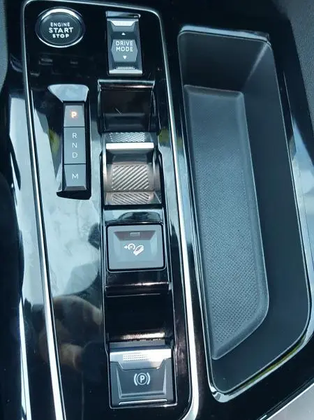 Vue rapprochée de la console centrale noire brillante du Peugeot 5008 2024, avec bouton start, sélecteur de boîte auto et frein à main électrique.