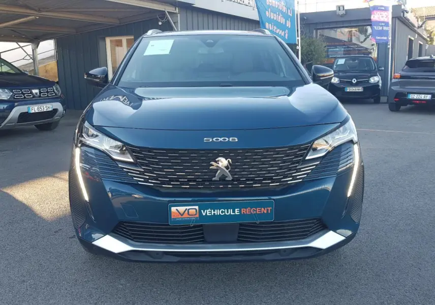 Vue frontale d’un Peugeot 5008 bleu 2024 avec calandre noire, feux LED allumés et plaque « Véhicule récent ».