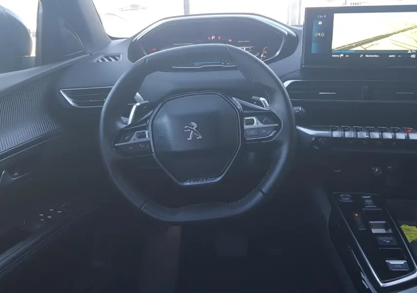 Vue intérieure centrée sur le volant cuir et le cockpit numérique du Peugeot 5008 2024, avec écran tactile et commandes modernes.