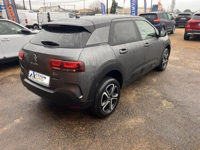 Vue 3/4 arrière droite d'une Citroën C4 Cactus gris Platinium avec jantes alliage et vitres teintées sur parking humide.