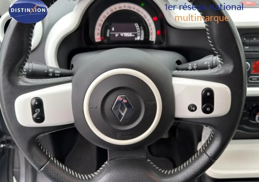 Vue rapprochée du volant cuir noir et blanc de la Renault Twingo III gris foncé, avec commandes intégrées visibles.