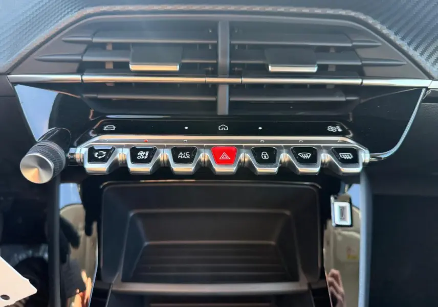 Gros plan sur la console centrale de la Peugeot 208 jaune 2025, montrant les commandes climatisation et boutons fonctionnels.