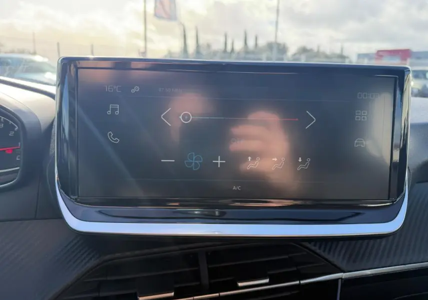 Écran tactile du tableau de bord de la Peugeot 208 jaune, vue frontale intérieure avec commandes climatisation visibles.