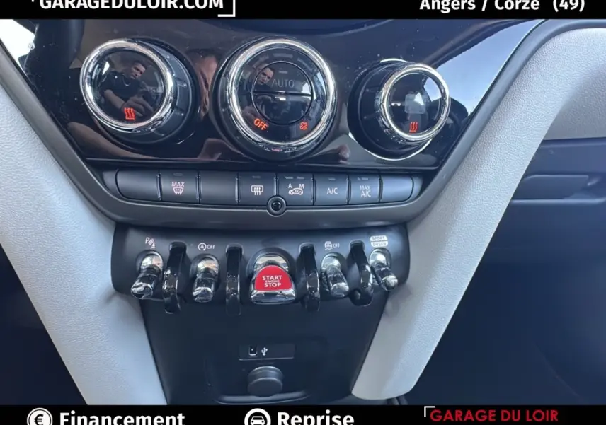 Gros plan sur la console centrale noire et grise du MINI Countryman bleu, avec boutons chrome et bouton start/stop rouge.