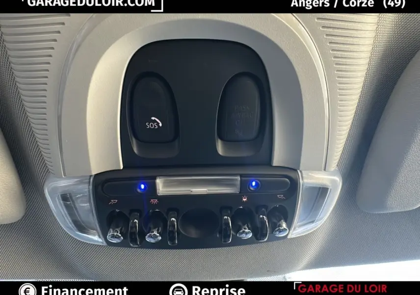 Vue en plongée sur la console de plafonnier intérieure grise avec interrupteurs chromés et voyants bleus allumés d'une MINI Countryman bleue.