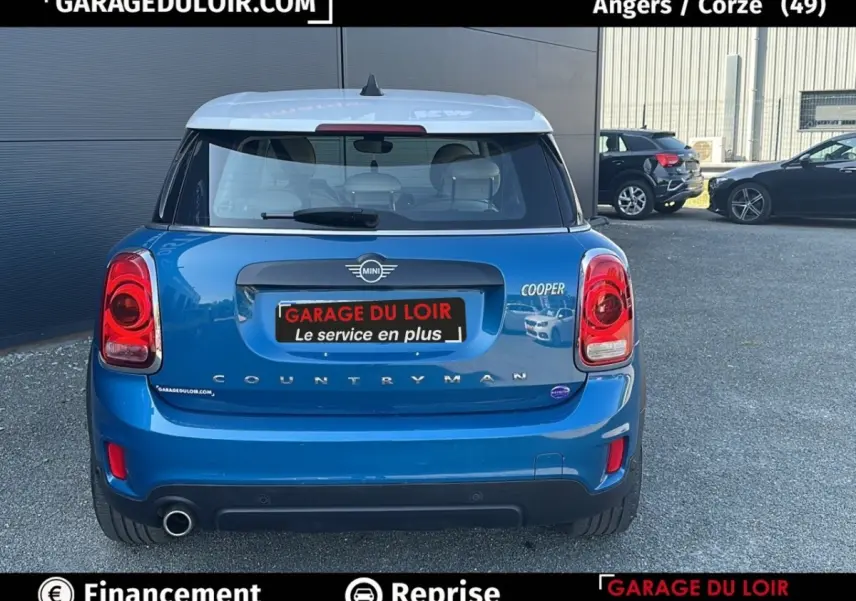 Vue arrière d'une MINI Countryman Cooper bleu avec toit blanc, feux rouges et double sortie d'échappement visible.