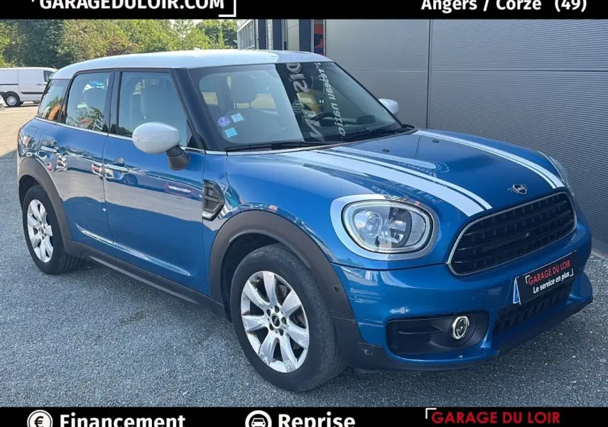Vue 3/4 avant d'une MINI Countryman Cooper Exquisite bleu avec toit blanc et bandes blanches sur le capot, garée sur un sol gravillonné.