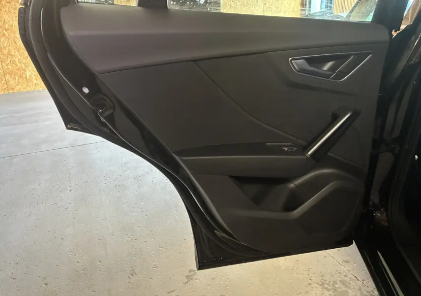 Vue intérieure de la porte arrière gauche noire de l'Audi Q2 2023 avec poignée et commande de vitre électrique.