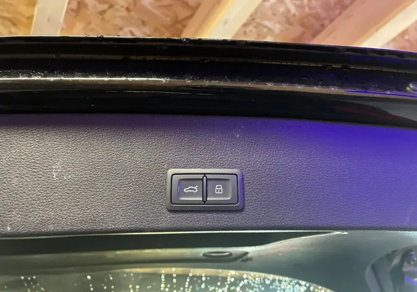 Gros plan sur les boutons d'ouverture et de verrouillage du coffre, intérieur noir du hayon d'un Audi Q2 noir.